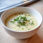 A creamy bowl of cauliflower soup topped generously with grated cheese and fresh chopped chives.