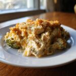 A serving of creamy Chicken Divan casserole with broccoli florets and a golden breadcrumb topping on a white plate.
