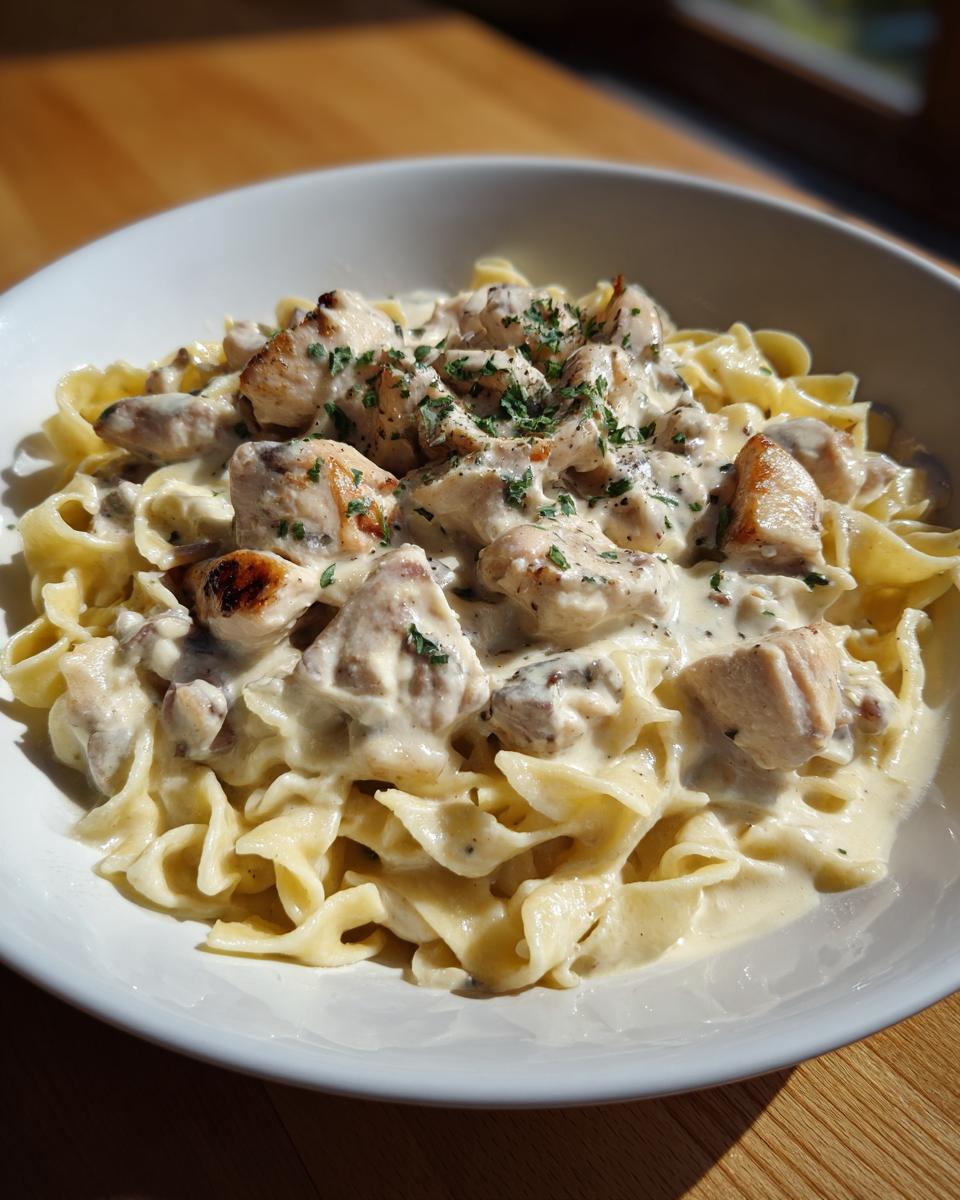 Close-up of a white bowl filled with creamy chicken pasta made with wide egg noodles and topped with herbs.