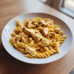 Close-up of creamy, orange-sauced chicken pasta made with fusilli noodles served in a white bowl.