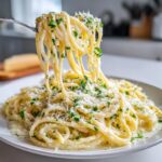 A fork lifts strands of creamy lemon pasta coated in sauce, topped with grated Parmesan and fresh parsley.