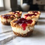 Close-up of creamy mini cheesecake bites with graham cracker crust and bright red jam topping.