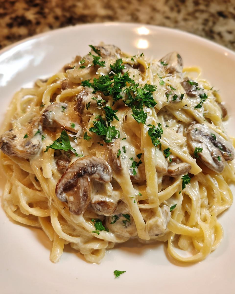 Close-up of creamy mushroom pasta (fettuccine style) topped with fresh parsley and grated cheese.