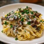 Close-up of creamy fettuccine mushroom pasta topped generously with sautéed mushrooms and fresh parsley.
