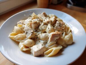 Close-up of a white bowl filled with creamy chicken pasta, featuring shell-shaped noodles and seasoned chicken pieces.