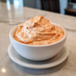 A close-up of thick, creamy orange burger sauce, swirled high in a small white dipping bowl.