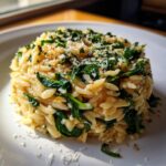Close-up of creamy orzo pasta mixed with wilted spinach, topped with grated cheese and herbs.