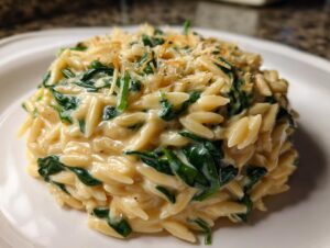 Close-up of a serving of creamy orzo pasta mixed with wilted spinach and topped with grated cheese.