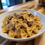 A close-up of creamy parmesan garlic beef bowtie pasta served in a white bowl on a wooden surface.