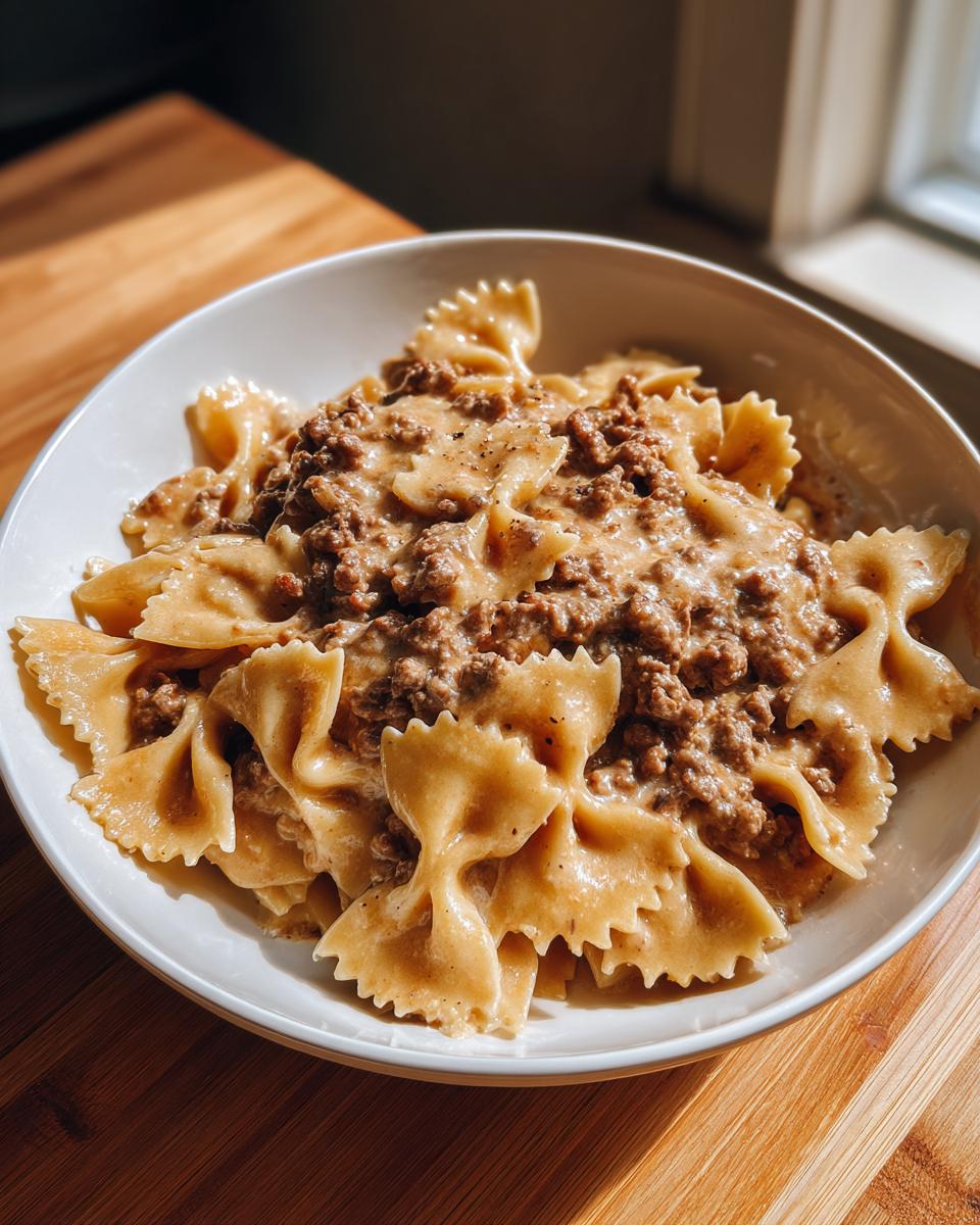A white bowl filled with creamy parmesan garlic beef bowtie pasta, served on a wooden surface.