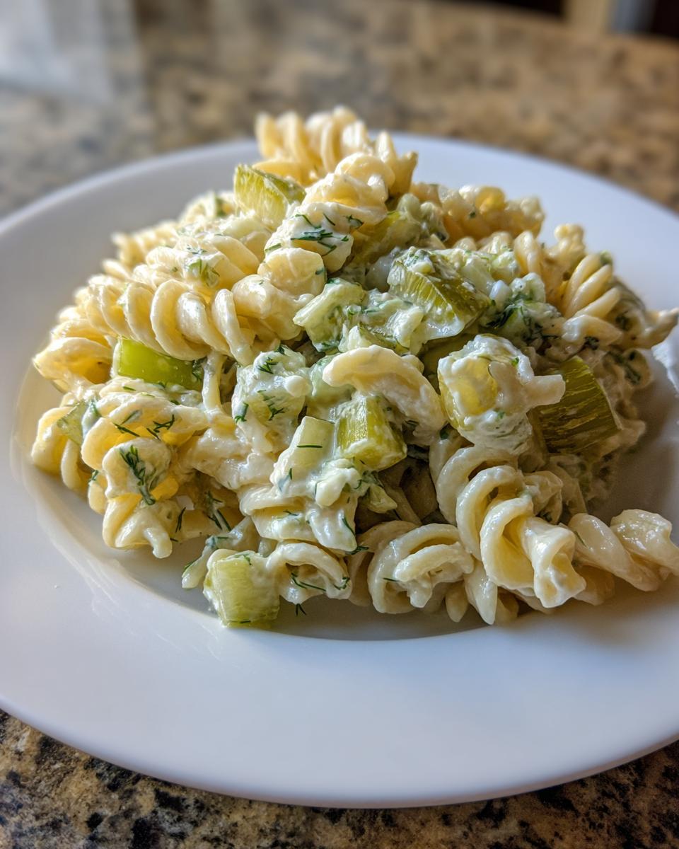 Close-up of creamy pickle pasta salad made with fusilli pasta, dill, and chopped pickles on a white plate.