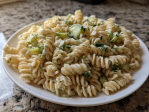 A close-up of creamy pickle pasta salad made with fusilli pasta and visible chunks of cucumber on a white plate.