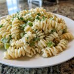 Close-up of creamy pickle pasta salad made with rotini pasta, visible chunks of green pickle, and fresh dill.