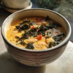 Close-up of a hearty bowl of Tuscan white bean soup featuring creamy broth, white beans, dark green kale, and diced tomatoes.