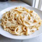 A close-up of fettuccine pasta generously coated in creamy vegan alfredo sauce and topped with black pepper.