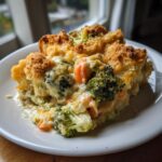 A close-up of a creamy vegetable casserole slice featuring broccoli and carrots with a golden, crispy topping.