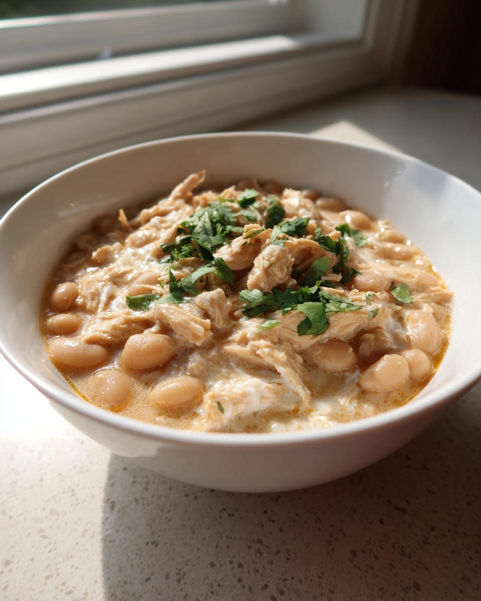 A close-up of a white bowl filled with creamy white chicken chili, featuring shredded chicken and white beans, topped with fresh cilantro.