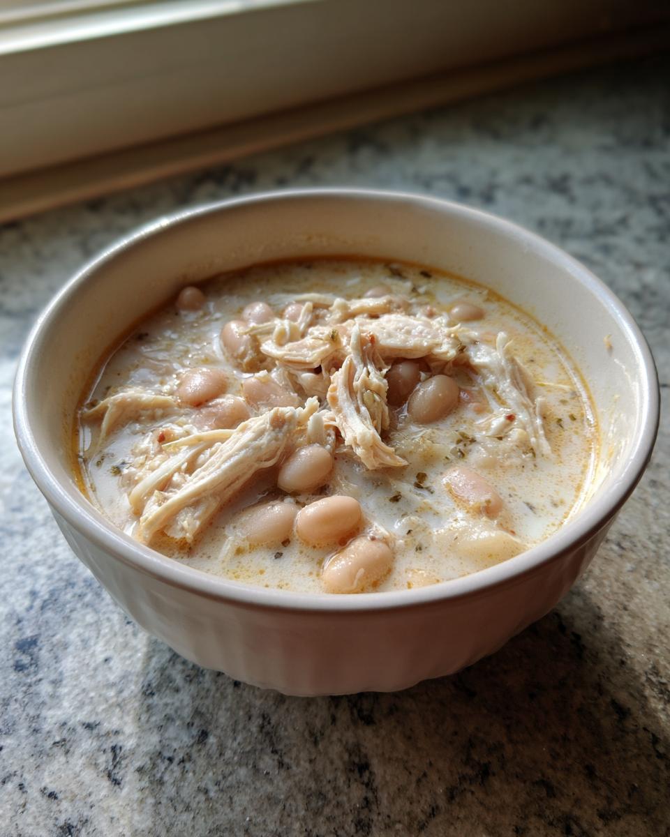 A close-up of a white bowl filled with creamy white chicken chili recipe, featuring shredded chicken and white beans.