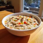 A close-up of a creamy bowl of amazing wild rice soup topped with shredded chicken, carrots, and celery.