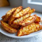 A close-up of golden brown, seasoned air fryer potato wedges piled high on a white plate.