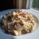 Close-up of creamy, shredded crockpot marry me chicken mixed with sun-dried tomatoes on a white plate.