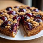 A close-up of a moist plum cake topped with streusel crumbs, with two slices already cut and slightly separated.
