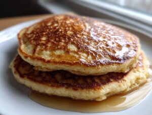Close-up of two fluffy almond flour pancakes stacked high, drizzled with golden syrup.