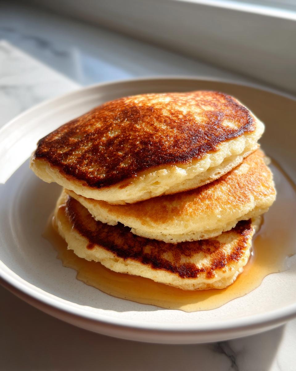 A stack of three fluffy almond flour pancakes drizzled with maple syrup on a light plate.