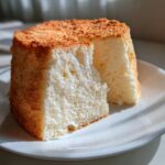 Close-up of a light and airy slice of angel food cake showing its white, spongy interior and golden-brown crust.