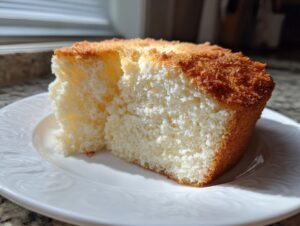 A close-up of a light and airy slice of angel food cake with a golden brown crust on a white plate.