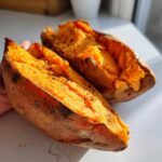 Two halves of fluffy baked sweet potatoes showing bright orange flesh seasoned with pepper.