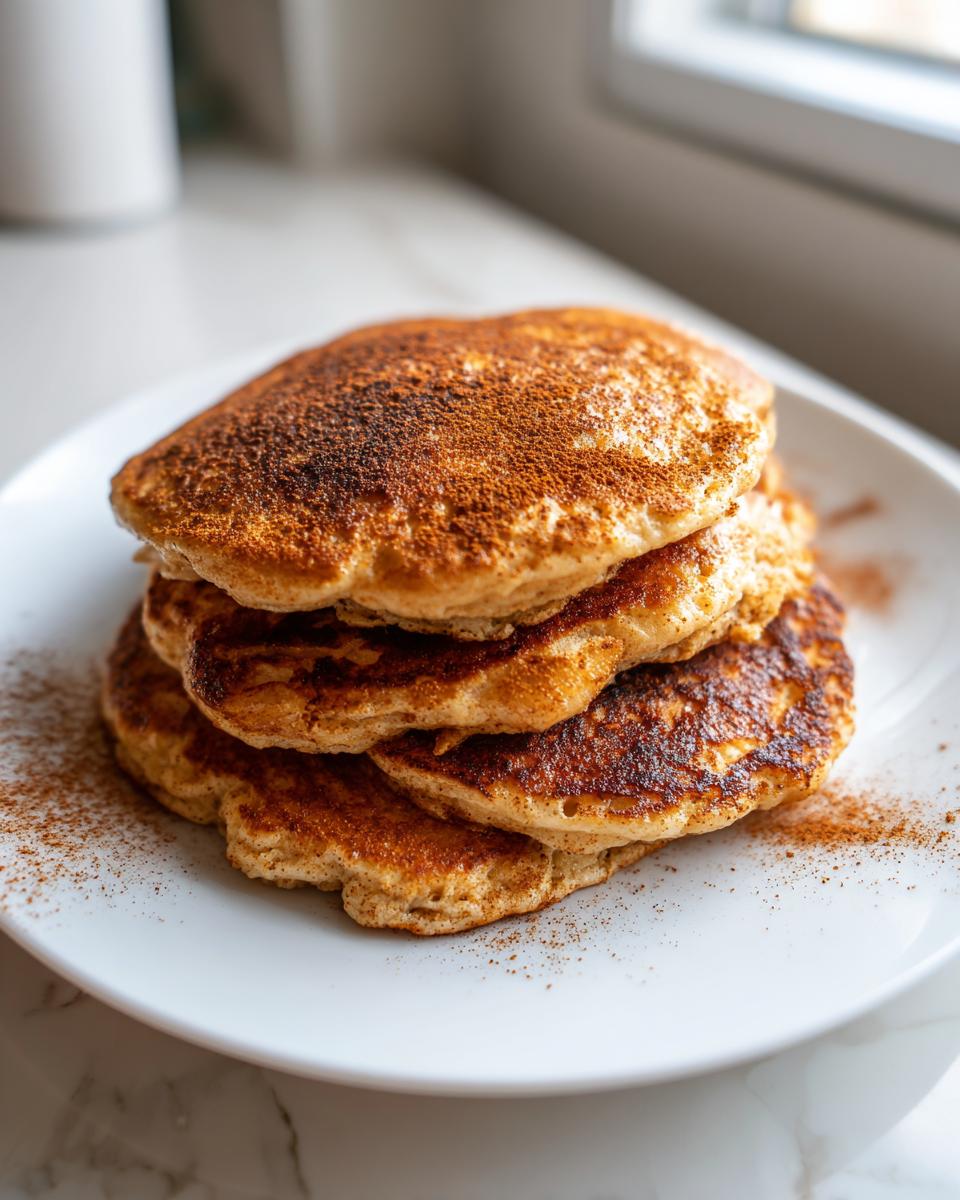 A stack of four fluffy banana oatmeal pancakes dusted generously with cinnamon on a white plate.