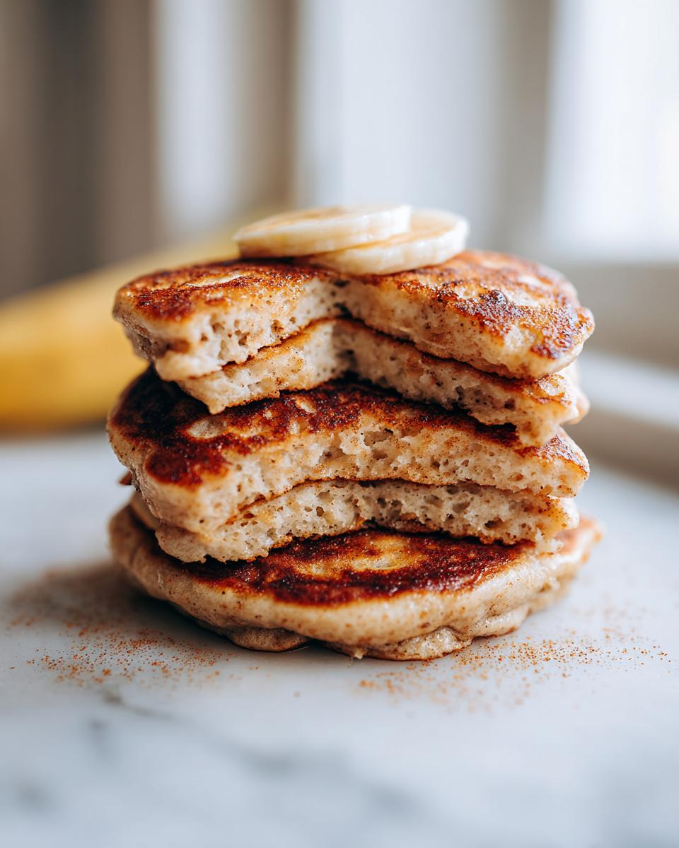 Close-up of a stack of fluffy banana oatmeal pancakes, cut in half to show texture, topped with banana slices.
