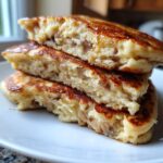 Close-up of three fluffy banana pancakes stacked and cut in half, showing the moist interior and drizzle of syrup.