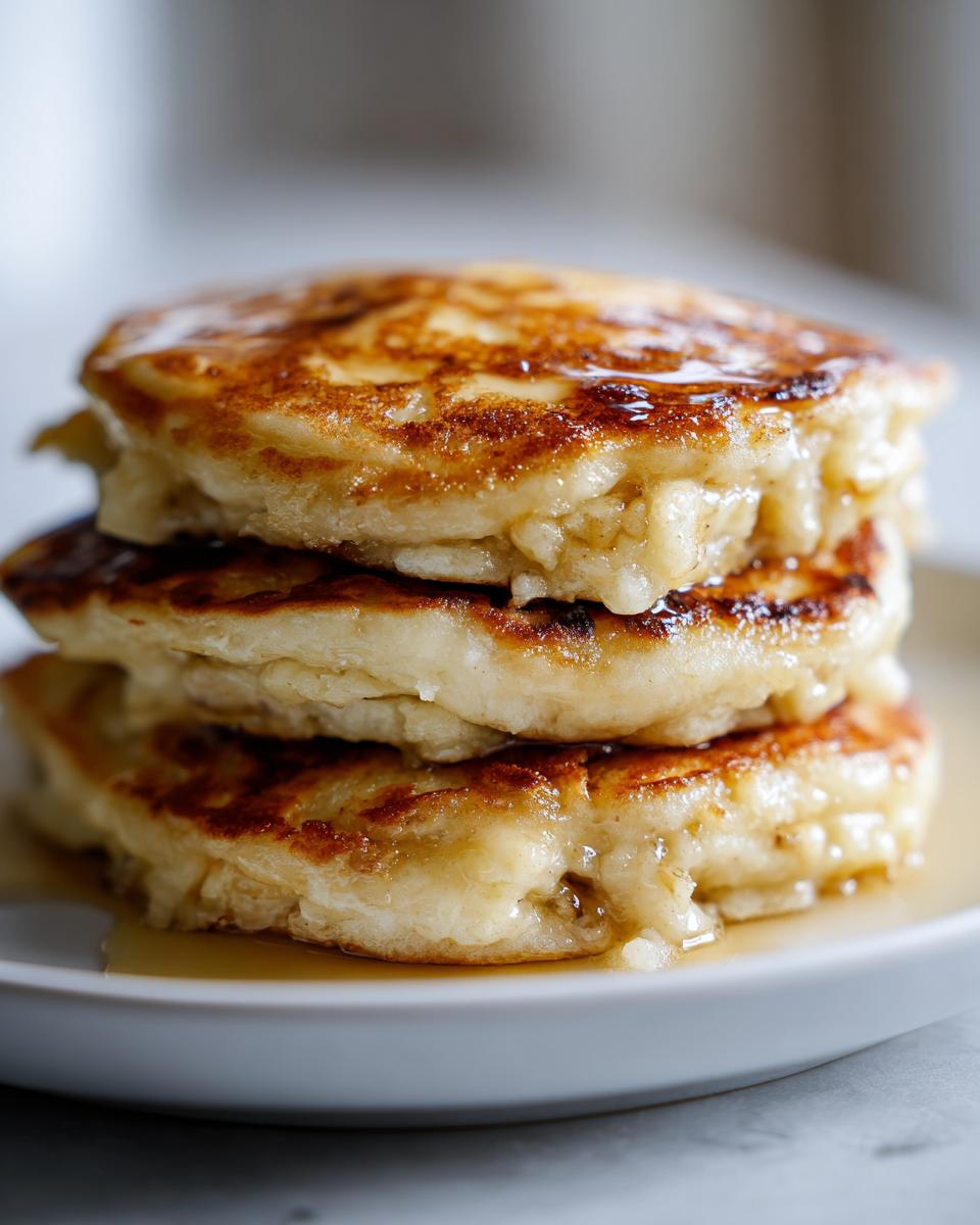Close-up of a tall stack of three fluffy banana pancakes, golden brown and dripping with syrup.