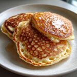 Close-up of three fluffy discard pancakes stacked on a plate, showing perfect air bubbles and a glossy honey drizzle.