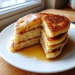 A stack of fluffy sourdough discard pancakes cut to show the airy interior, drizzled generously with maple syrup.