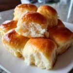 A stack of freshly baked, glossy sweet potato rolls, one torn open to show the soft interior.