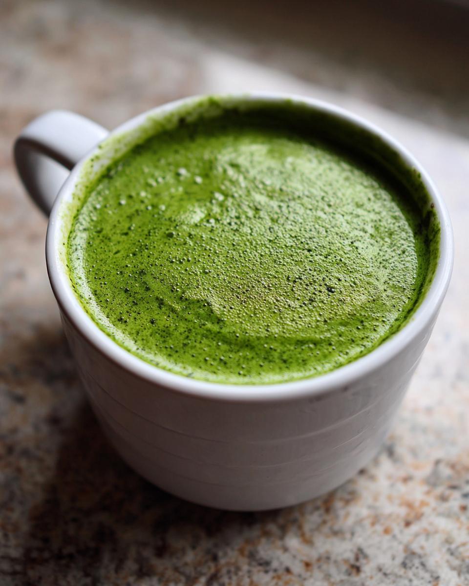 Close-up of bright green, foamy spinach soup served hot in a white mug.