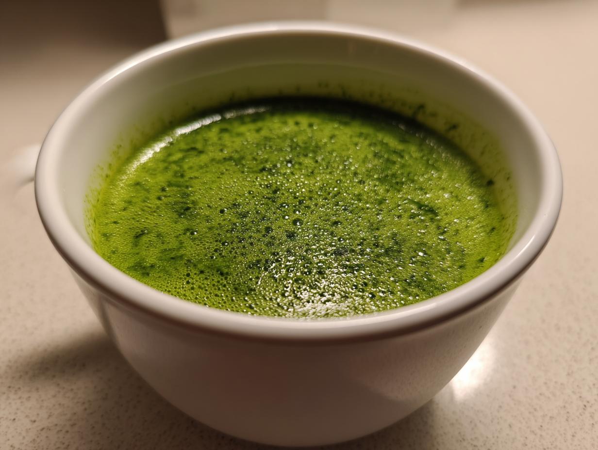 Close-up view of vibrant green, slightly foamy spinach soup served in a white ceramic mug.