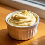Close-up of thick, creamy hollandaise sauce swirled beautifully in a small white ramekin.