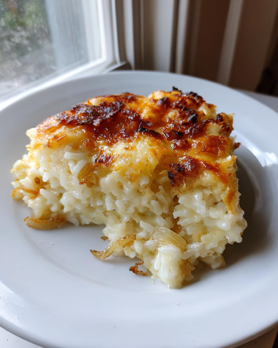 A square serving of creamy french onion butter rice topped with deeply browned, melted cheese.