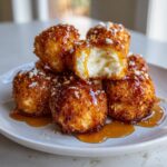 A stack of crispy, golden-brown fried goat cheese balls drizzled with honey, one is broken open showing the creamy interior.