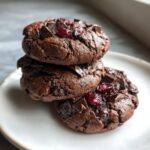 A stack of three fudgy chocolate cherry cookies topped with chocolate chunks and dried cherries.