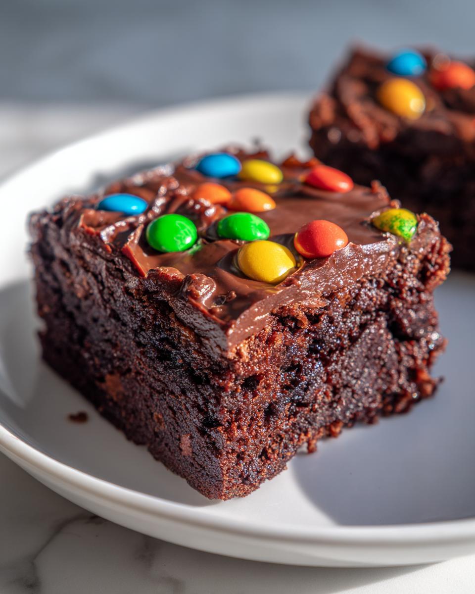 A close-up of a rich, fudgy square of cosmic brownies topped with chocolate frosting and colorful candy pieces.
