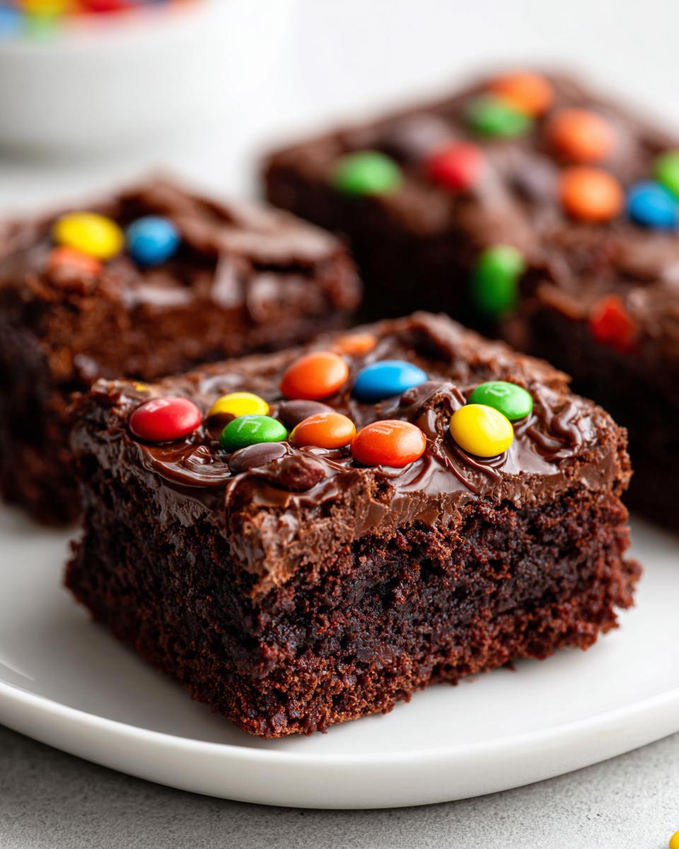 A close-up of a fudgy square of cosmic brownies topped with chocolate frosting and colorful candy-coated chocolates.