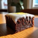 Close-up of a fudgy, dark chocolate lemon brownies square topped with white glaze and lemon zest.