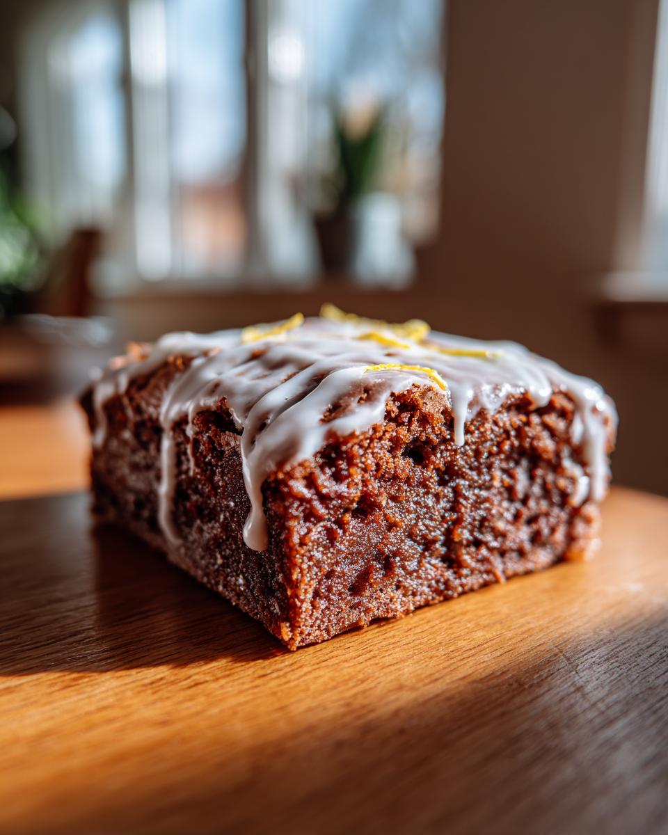 A close-up of a fudgy, dark slice of lemon brownies topped with white glaze and zest.