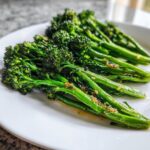 Close-up of bright green, tender stalks of garlic lemon broccolini glistening with sauce on a white plate.