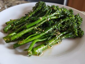 A close-up of bright green, cooked broccolini seasoned with garlic and lemon, served on a white plate.